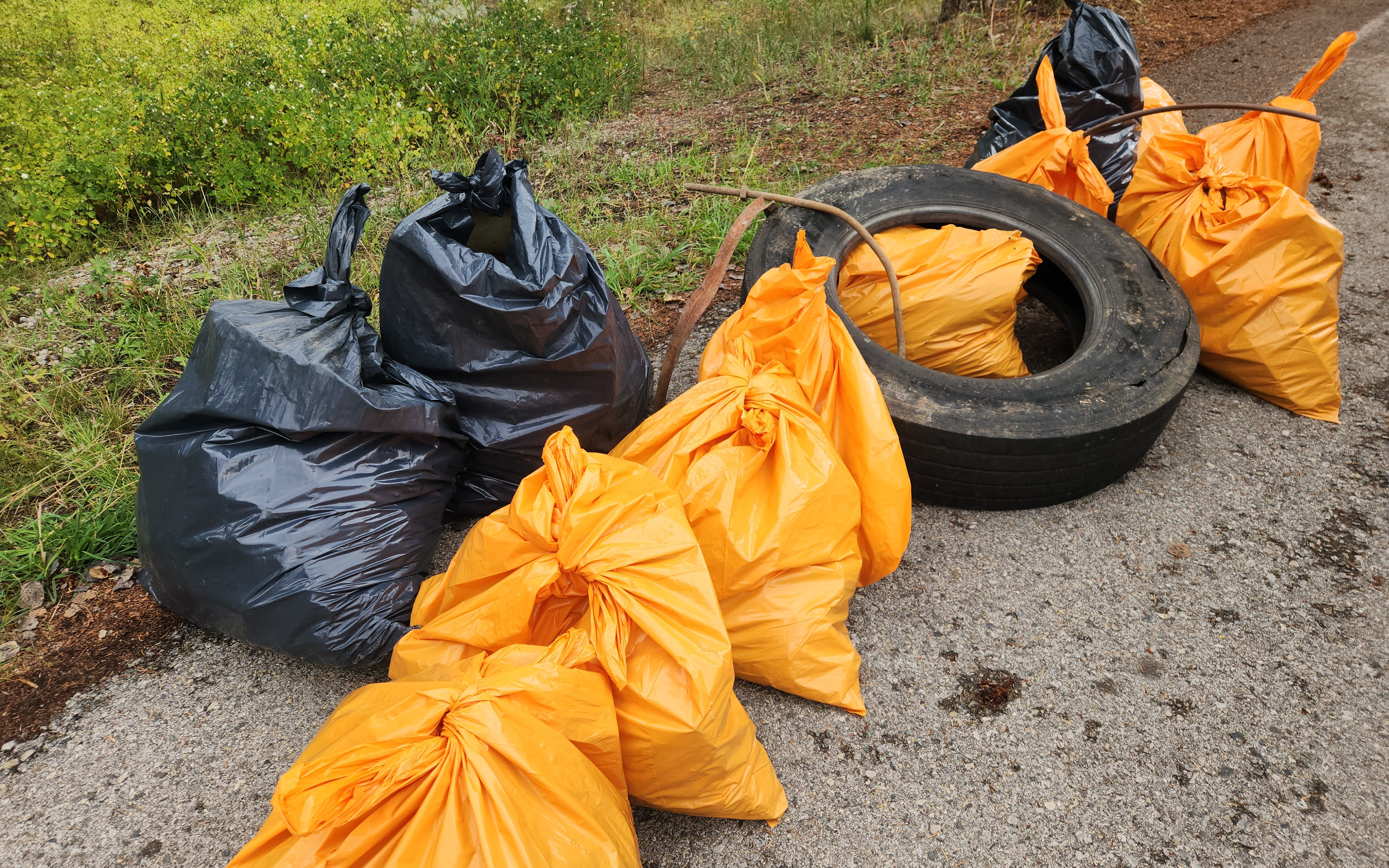 Full trash bags gathered together along with larger pieces of metal and an old tire